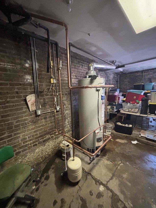 Installed a 100-gallon tanked water heater in basement utility room with complete copper piping connections and white expansion tank positioned at base of unit. All supply and discharge lines were properly configured with appropriate valves and fittings, and system was tested for proper operation and leak-free connections upon completion.