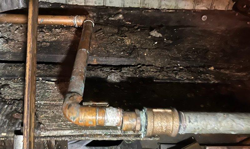 Responded to water leak caused by failed soldered joint on copper piping in basement crawl space. The original solder connection had separated, resulting in active water discharge. Assessed surrounding copper plumbing system showing significant age-related corrosion and oxidation. Repaired the compromised joint and inspected adjacent piping for structural integrity. Noted deteriorated wooden support beams and joists displaying moisture damage throughout the work area, which may require future attention to prevent further plumbing complications.