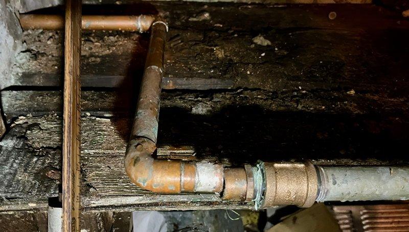 Responded to water leak caused by failed soldered joint on copper piping in basement crawl space. The original solder connection had separated, resulting in active water discharge. Assessed surrounding copper plumbing system showing significant age-related corrosion and oxidation. Repaired the compromised joint and inspected adjacent piping for structural integrity. Noted deteriorated wooden support beams and joists displaying moisture damage throughout the work area, which may require future attention to prevent further plumbing complications.