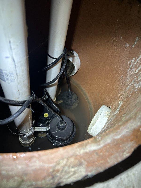 Performed comprehensive sump pump inspection per customer request. Evaluated pump operation, electrical functionality, and overall system condition. Visual inspection revealed significant mineral deposits and hard water staining throughout the basin walls, indicating prolonged exposure to high mineral content water. Sump pump assembly showed normal wear consistent with regular use, with float switch mechanism and discharge piping intact. Tested electrical voltage at pump, recording 135 volts to verify proper power supply. Observed standing water in basin with pump components functioning as designed. Documented system condition with photographs for customer records, noting mineral buildup on basin surfaces and general maintenance status of pump assembly and discharge configuration.