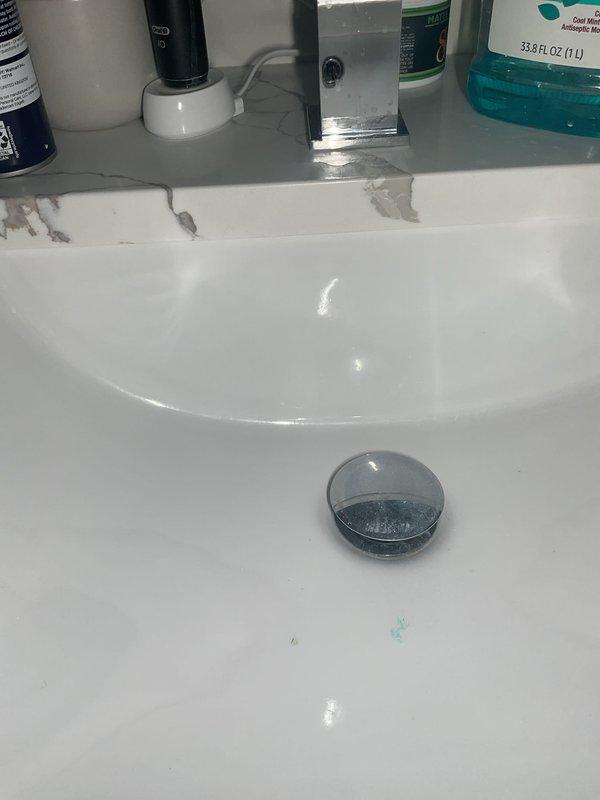 Responded to service call for slow-draining bathroom sink that was filling up with water during use. Upon inspection, found white porcelain sink with visible pooling water and drainage issues. Examined sink basin, drain stopper assembly, and chrome fittings. Assessed under-sink plumbing configuration, including white PVC P-trap assembly, water supply lines with braided hoses, and wall-mounted shut-off valves. Documented existing condition showing aged sink with chipped finish along back edge near faucet area. Evaluated drainage system components to identify source of blockage causing water backup and slow drainage in bathroom sink.