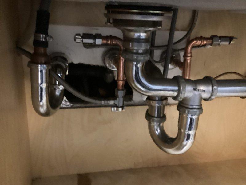 Completed dual-sink angle stop replacement under kitchen cabinet following coordinated building shutdown. Removed existing twin angle stops from 1/2" threaded nipples and installed new copper supply piping configuration with four angle stops—two for hot water supply and two for cold water supply. After installation, building management restored water pressure to lines, and all connections were thoroughly inspected and verified leak-free before returning system to service.