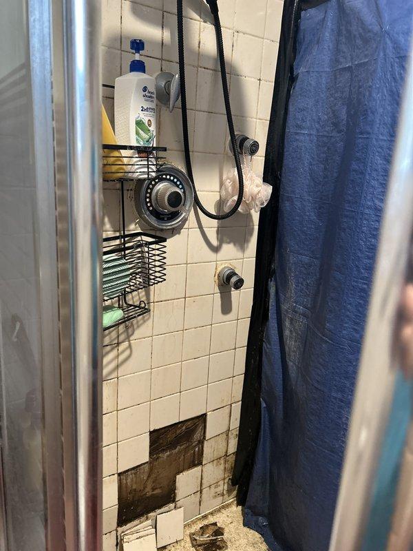 Responded to a multi-issue plumbing service call at a century-old residence to address a long-standing shower leak, investigate water damage from an upstairs pipe leak affecting the downstairs ceiling, and diagnose a slow-filling toilet.

Upon arrival, conducted a comprehensive inspection of the shower stall and identified significant water damage at the base of the tiled shower wall where tiles had been removed or fallen away, exposing deteriorated substrate material behind the tile assembly. The shower fixture and surrounding tile work showed signs consistent with chronic moisture intrusion. Assessed the handheld shower system and wall-mounted controls for potential leak sources.

Proceeded to the downstairs ceiling area directly below the suspected upstairs pipe leak. Documented extensive water damage evidenced by widespread dark speckling and staining across the ceiling surface, with heavier concentration in specific areas indicating active or recent moisture exposure. An existing 