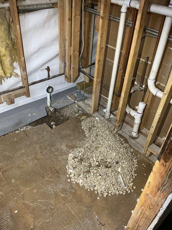 Completed plumbing rough-in installation for under-construction residential space, including PVC drainage system installation with proper pipe mounting and securing to wooden framing. Applied leveling aggregate and prepared subfloor surface for final plumbing fixture placement, with all supply and waste lines positioned according to specifications.