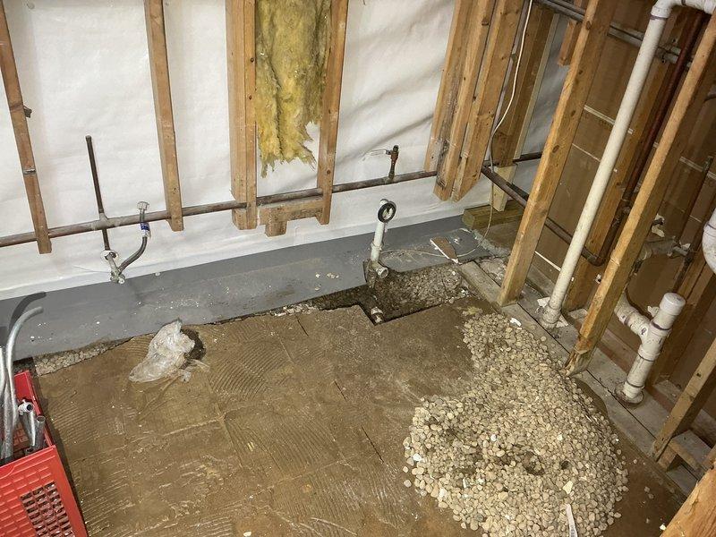 Completed plumbing rough-in installation for under-construction residential space, including PVC drainage system installation with proper pipe mounting and securing to wooden framing. Applied leveling aggregate and prepared subfloor surface for final plumbing fixture placement, with all supply and waste lines positioned according to specifications.