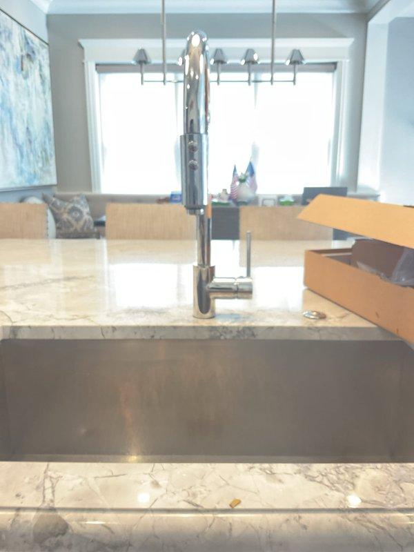 Initiated installation of professional-style chrome kitchen faucet with pull-down sprayer on marble countertop island and installed new garbage disposal unit with connected PVC P-trap drainage system. Work remains incomplete per customer request for different technician to return and finalize installation and collect payment.