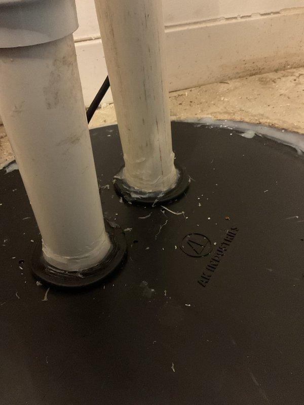 Responded to callback for improperly sealed ejector basin. Upon inspection, found standing water and debris accumulation in basin with rust-colored staining along seams and corners, indicating seal failure at basin perimeter. Observed two PVC discharge pipes extending through rubber sealing boot with visible moisture and residue around edges, confirming inadequate seal at pipe penetrations. Re-sealed ejector basin assembly and pipe penetrations to manufacturer specifications to prevent future water infiltration and ensure proper wastewater containment.