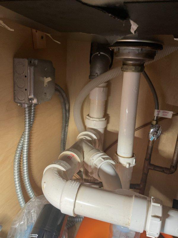 Responded to drainage issue affecting kitchen sink, dishwasher, and garbage disposal in century-old home. Inspected plumbing assembly beneath double-basin sink, including PVC P-trap configuration, tailpiece connections, and horizontal drain line routing to wall. Assessed electrical connections at junction box and flexible conduit servicing disposal unit. Documented existing plumbing configuration showing standard white PVC trap assembly with proper water seal formation. Evaluated drainage pathway affecting both appliances to determine cause of month-long backup condition and provided recommendations for resolution.