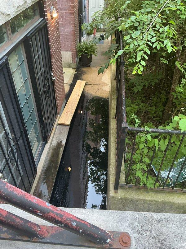 Responded to callback regarding exterior drainage and sump pump system. Upon arrival, found significant standing water accumulation in below-grade stairwell/passageway between buildings, indicating drainage failure. Inspected interior sump pump basin and discovered heavy sediment buildup and debris accumulation affecting pump operation. Basin showed extensive dirt and grime around edges with visible signs of reduced pumping efficiency. Documented existing conditions of copper discharge piping showing oxidation and PVC drain lines. Photographed flooded exterior access area and compromised sump system for customer records and follow-up recommendations.