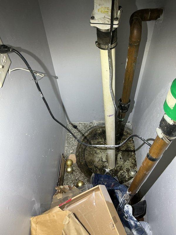 Responded to callback regarding exterior drainage and sump pump system. Upon arrival, found significant standing water accumulation in below-grade stairwell/passageway between buildings, indicating drainage failure. Inspected interior sump pump basin and discovered heavy sediment buildup and debris accumulation affecting pump operation. Basin showed extensive dirt and grime around edges with visible signs of reduced pumping efficiency. Documented existing conditions of copper discharge piping showing oxidation and PVC drain lines. Photographed flooded exterior access area and compromised sump system for customer records and follow-up recommendations.