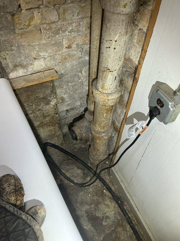 Conducted comprehensive assessment of main sewer line from house to municipal connection, water supply line, and catch basin drainage system in 130-year-old residential property. Inspected basement utility area revealing aged cast iron waste piping with visible corrosion, existing PVC drainage modifications, and deteriorated concrete foundation walls showing efflorescence and moisture intrusion. Documented existing plumbing infrastructure including corroded vertical stack, laundry drainage system, and copper water supply lines to provide detailed replacement estimates for main sewer lateral, water service line upgrades, and catch basin repairs necessary to address aging infrastructure concerns.