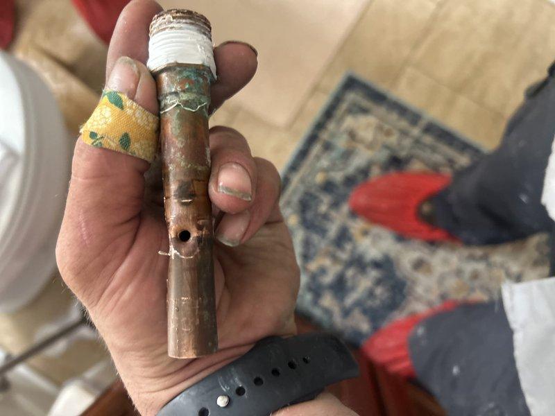 Responded to report of leak behind shower in bathroom with alcove-style tub installation. Upon inspection, identified severely corroded copper supply pipe with visible perforation causing water leakage. Removed damaged section of pipe showing extensive rust deterioration and compromised structural integrity. Replaced failed copper piping with new materials to restore proper water supply function and eliminate leak condition.