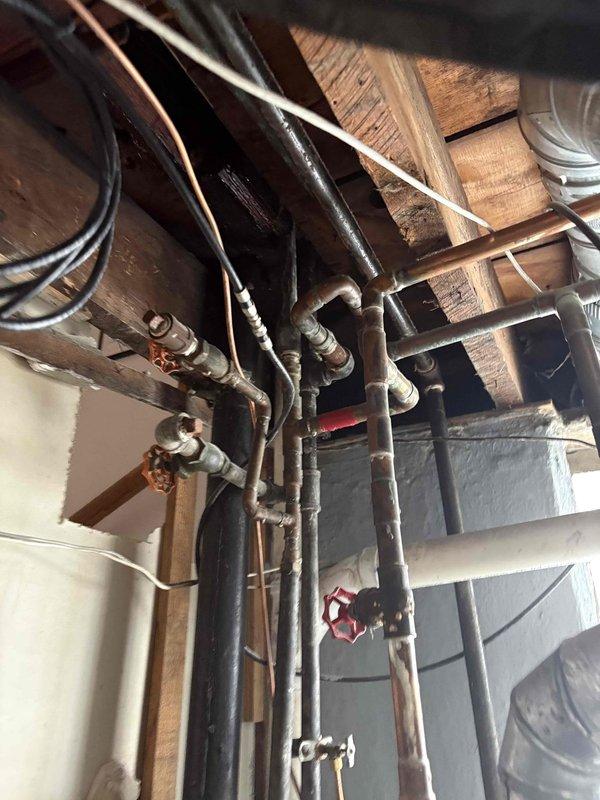 Responded to service call for failed water supply line serving second floor laboratory faucet. Upon inspection, identified pinhole leak in vertical copper riser running from basement through ceiling joists to second floor. Documented existing piping configuration including multiple shut-off valves, copper supply lines, and connection points within exposed basement ceiling infrastructure. Assessed extent of damage and determined complete re-pipe from basement origin to second floor laboratory fixture required due to compromised pipe integrity. Photographed affected piping system showing riser location, valve positions, and routing path through structural joists to stairway area leading to second floor. Prepared estimate for replacement of vertical water supply line including removal of damaged copper piping, installation of new riser, and restoration of water service to laboratory faucet.