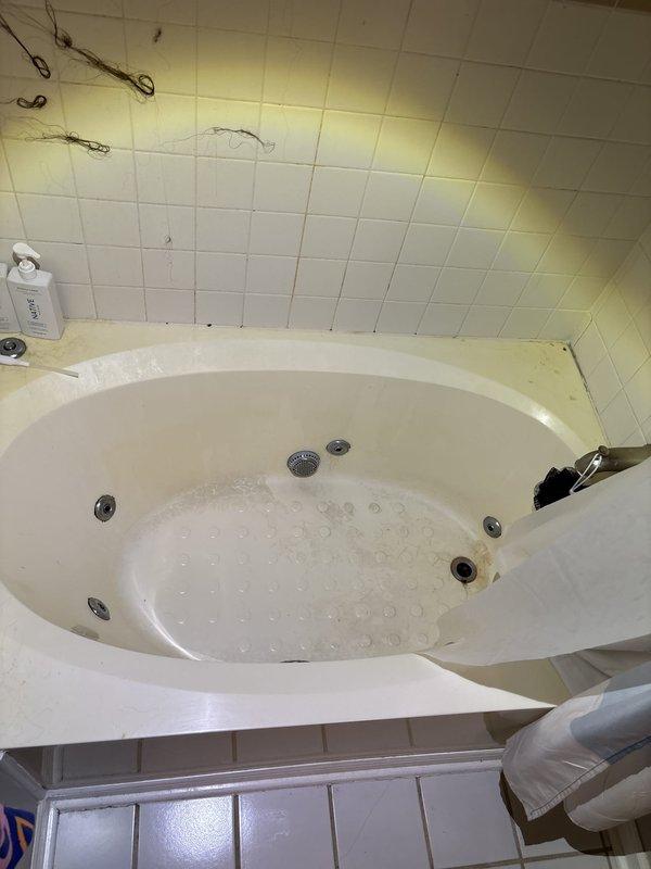 Responded to water leak originating from unit and affecting the unit below. Upon arrival, inspected jetted bathtub and surrounding bathroom fixtures to identify source of leak. Documented existing conditions including water damage and staining visible on wall tiles and ceiling surfaces near tub area. Examined toilet installation and floor mounting points for potential leak sources. Photographed affected areas showing standing water in jetted tub with active jet fixtures, deteriorated grout lines, and water-stained ceiling tiles indicating ongoing moisture intrusion. Coordinated authorization and provided assessment for necessary repairs to resolve inter-unit water leak issue.