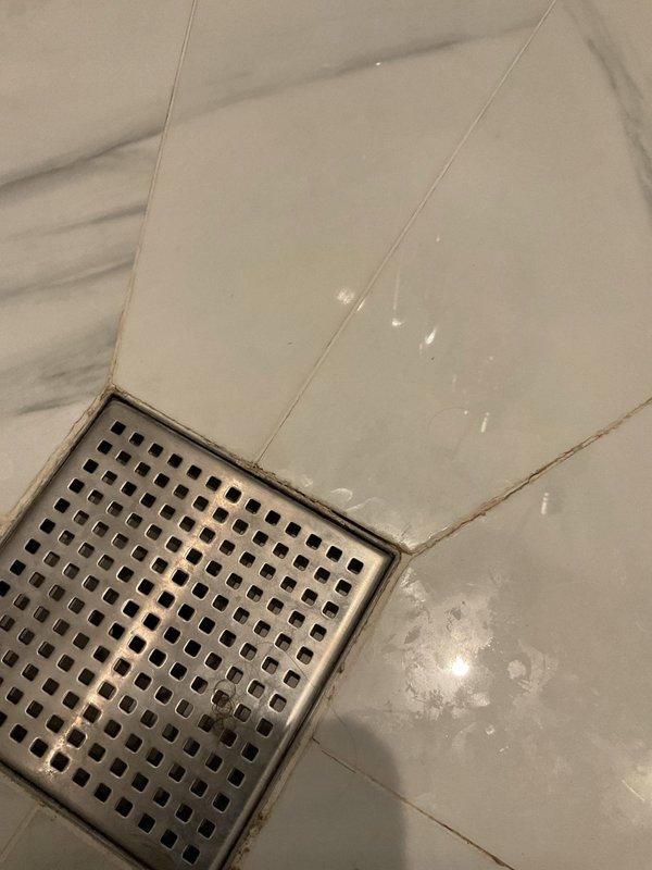 Responded to water leak complaint affecting kitchen ceiling below bathroom. Performed thorough inspection of shower area to locate source of water intrusion. Examined shower floor drain, tile installation, and grout integrity in bathroom with marble-effect porcelain tile flooring. Documented conditions of floor drain assembly, tile surfaces, and grout lines for further assessment of potential leak pathways causing ceiling damage below.