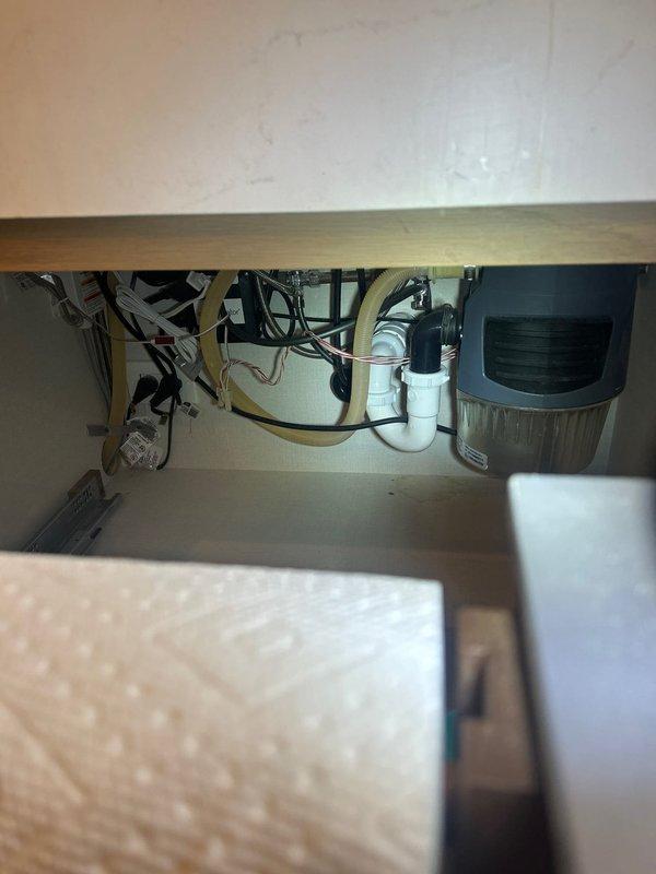 Installed new garbage disposal unit under kitchen sink with complete plumbing assembly including white PVC P-trap and drain connections. Completed all electrical wiring connections with proper wire nuts, installed flexible discharge tubing, and verified system operation with no leaks detected.