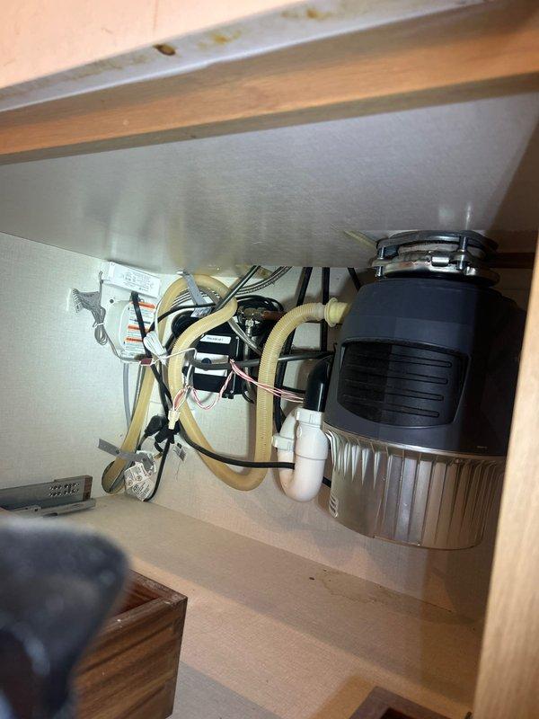 Installed new garbage disposal unit under kitchen sink with complete plumbing assembly including white PVC P-trap and drain connections. Completed all electrical wiring connections with proper wire nuts, installed flexible discharge tubing, and verified system operation with no leaks detected.