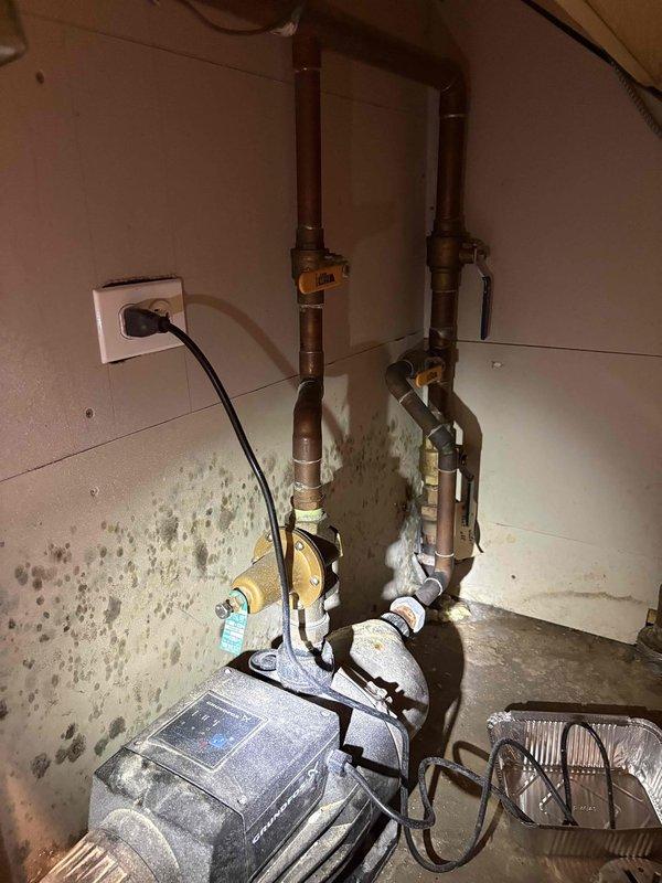 Responded to reported water leak in downstairs utility room affecting adjacent garage area. Upon inspection, identified failed seal on booster pump system responsible for transferring water to upper floor levels. Pump unit showed signs of prolonged moisture exposure with visible water staining on concrete floor and significant mold growth on surrounding walls, consistent with reported two-week leak duration. Assessed copper piping connections, pressure gauges, and brass fittings for integrity. Documented extensive water damage to utility room surfaces and pump installation area. Photographed existing conditions including deteriorated wall surfaces, floor staining, and overall pump configuration for service records. Provided recommendations for pump seal replacement, mold remediation of affected wall surfaces, and evaluation of drainage solutions to prevent future water accumulation in utility space.