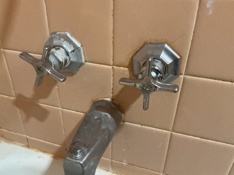 # Bathtub Fixture Replacement and Rust Remediation

Responded to service call for aging bathtub fixtures with visible rust staining and mineral buildup. Removed and replaced deteriorated chrome tub spout and dual-handle valve assembly that were causing discoloration on the tub surface and surrounding tile grout. Addressed rust-colored mineral deposits and water staining present on the bathtub basin below the spout. Cleaned affected tile surfaces and grout lines around fixture mounting points to remove accumulated mineral deposits and corrosion. Installed new chrome-plated fixtures with proper sealing to prevent future water intrusion behind escutcheon plates. Verified proper water flow and tested valve operation to ensure leak-free performance.
