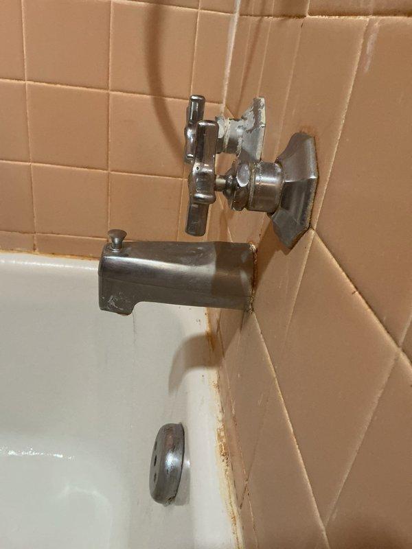# Bathtub Fixture Replacement and Rust Remediation

Responded to service call for aging bathtub fixtures with visible rust staining and mineral buildup. Removed and replaced deteriorated chrome tub spout and dual-handle valve assembly that were causing discoloration on the tub surface and surrounding tile grout. Addressed rust-colored mineral deposits and water staining present on the bathtub basin below the spout. Cleaned affected tile surfaces and grout lines around fixture mounting points to remove accumulated mineral deposits and corrosion. Installed new chrome-plated fixtures with proper sealing to prevent future water intrusion behind escutcheon plates. Verified proper water flow and tested valve operation to ensure leak-free performance.