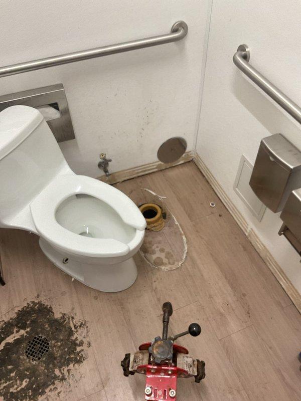 Conducted comprehensive drain and sewer assessment for commercial restroom facility experiencing plumbing issues. Inspection revealed active water leakage at toilet base with visible moisture staining on vinyl flooring, indicating compromised wax ring seal or flange connection. Evaluated exposed water supply lines, shutoff valves, and brass fixtures behind toilet for proper operation and potential leak sources. 

Assessed floor drain assembly installed in subflooring, noting weathered plywood surface and existing caulk seal around drain flange. Documented condition of drain components including inner opening, brass ring, and metallic collar for permanent repair recommendations. Photographed all affected areas including ADA-compliant accessible restroom features, exposed plumbing connections, and areas of water damage for estimate documentation. Scheduled follow-up appointment to present permanent solution options and implement necessary repairs to resolve water intrusion issues and res