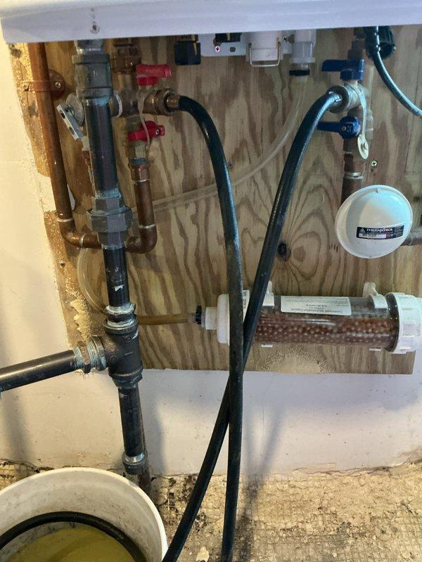 # Plumbing Maintenance - VIP Completed

Performed comprehensive plumbing systems maintenance on a 125-year-old residential property, with specific focus on inspecting and servicing neutralizers installed on both the hot water heater and furnace systems. Upon arrival, conducted thorough visual inspection of all accessible plumbing components throughout the service area.

Inspected the condensate neutralizer systems serving both the heating appliances. Examined the neutralizer bucket containing the neutralizing media, noting the presence of discharged condensate water with characteristic discoloration indicating active neutralization process. Verified proper operation of condensate drain lines feeding into the neutralizer system, with black flexible hoses properly submerged in the neutralizing solution. Assessed the condition of the neutralizing media and determined adequate levels present for continued effective operation.

Evaluated the plumbing infrastructure supporting the neutralize