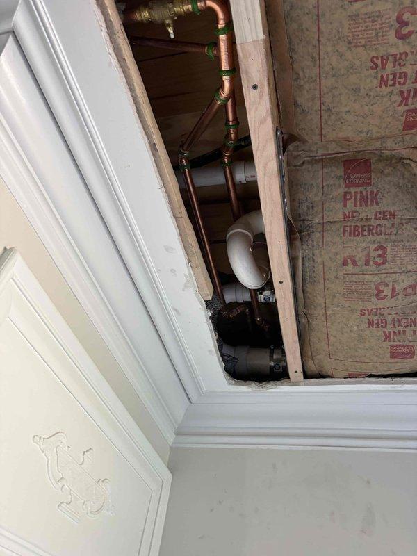 Responded to warranty call for disconnected water lines discovered during ceiling repair work. Upon inspection, found copper supply lines with brass fittings and shutoff valves were not properly connected beneath the floor system. Accessed plumbing through ceiling cavity opening, documented existing conditions showing exposed copper piping with green-capped valves running vertically through wall cavity between studs. Photographed installation to verify warranty claim and document pre-existing condition of disconnected water supply lines within the framed structure.