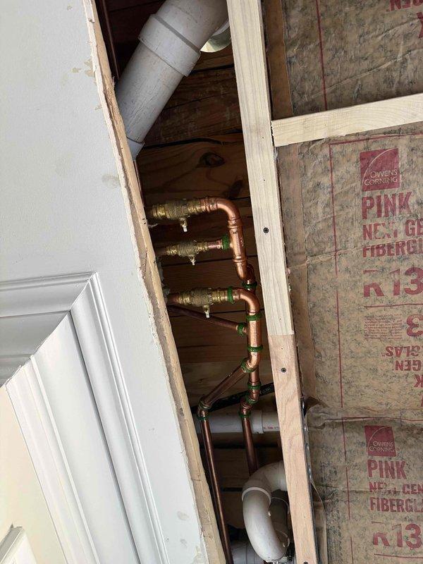 Responded to warranty call for disconnected water lines discovered during ceiling repair work. Upon inspection, found copper supply lines with brass fittings and shutoff valves were not properly connected beneath the floor system. Accessed plumbing through ceiling cavity opening, documented existing conditions showing exposed copper piping with green-capped valves running vertically through wall cavity between studs. Photographed installation to verify warranty claim and document pre-existing condition of disconnected water supply lines within the framed structure.