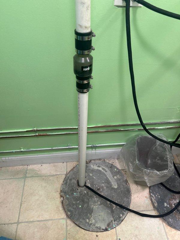 Conducted comprehensive assessment of existing sump and ejector pump system requiring replacement due to code violations and water backup issues through piping. Evaluated pit conditions requiring cleaning and documented non-compliant plumbing installation with white PVC discharge piping. Inspected utility sink area and associated drainage connections, noting improper venting and discharge configuration. Photographed sump pump basin with cover plate, vertical discharge assembly with multiple clamps and connectors, and electrical wiring routing for replacement specifications. Provided detailed estimate for complete system replacement including proper pit cleaning, code-compliant installation of new sump and ejector pumps, and correction of backflow issues.