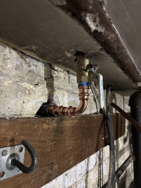 Replaced exterior hose spigot with new chrome-plated fixture featuring green wheel-style handle. Installation included connecting new brass ball valve with blue handle to existing copper supply line in basement, creating proper L-shaped configuration for optimal water flow and shutoff capability.