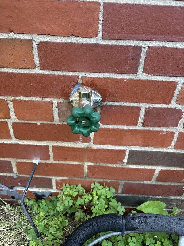Replaced exterior hose spigot with new chrome-plated fixture featuring green wheel-style handle. Installation included connecting new brass ball valve with blue handle to existing copper supply line in basement, creating proper L-shaped configuration for optimal water flow and shutoff capability.