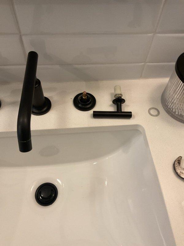 Responded to service call for Kohler bathroom sink faucet with detached cold side handle. Upon arrival, inspected the undermount basin with matte black fixtures and found the left handle had separated from its mounting base. Assessed all faucet components including escutcheon plate, spout assembly, and mounting hardware to determine repair requirements. Documented existing conditions with photographs showing disassembled fixture components and provided estimate for necessary repairs or replacement options.
