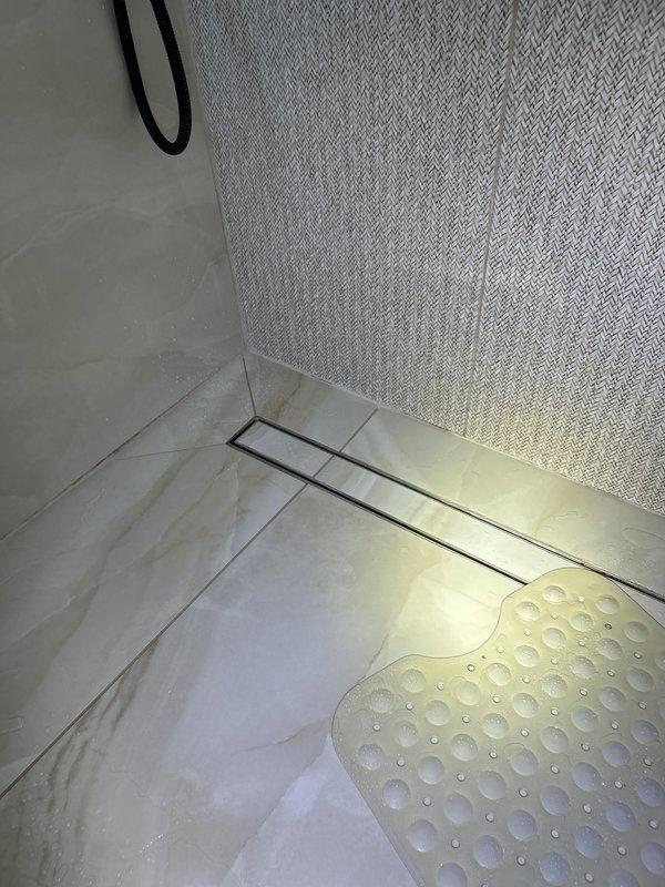 Responded to a water leak originating from the second floor and penetrating into the first floor below. Investigated the shower area as the suspected source of the leak, which had caused extensive water damage and potential mold growth. Performed visual inspection and documentation of the shower pan, linear drain assembly, and surrounding tile work to identify points of water intrusion. Photographed the shower floor, drain system, and wall surfaces showing the marble tile flooring, linear drain installation, and textured wall materials for diagnostic purposes and future remediation planning.