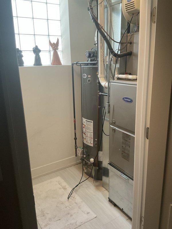 Completed same-day water heater installation in residential utility closet adjacent to existing Carrier furnace system. Installed new residential gas water heater with power vent exhaust system, including white flue connector and electric blower assembly. Connected copper water supply lines, configured gas valve and thermostat controls, and ensured proper combustion air intake through base ventilation louvers. All connections tested and verified operational.