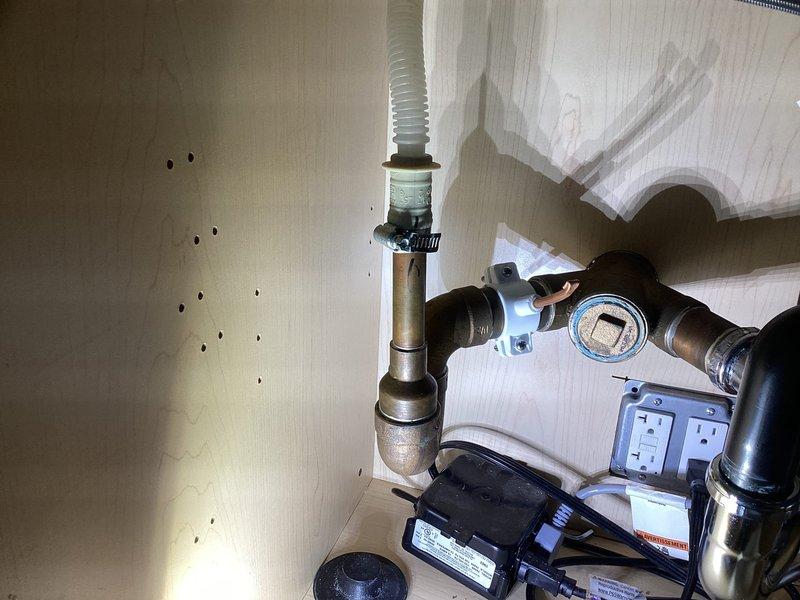 Completed installation of modern kitchen sink fixture system including undermount charcoal composite basin with dual faucet configuration featuring chrome and brushed nickel finishes. Installed comprehensive under-sink plumbing assembly with copper supply lines, black plastic fittings, pressure regulation system with digital monitoring gauge, integrated electrical outlet box, and pump unit with flexible discharge hose, ensuring all components meet code requirements and proper water flow functionality.