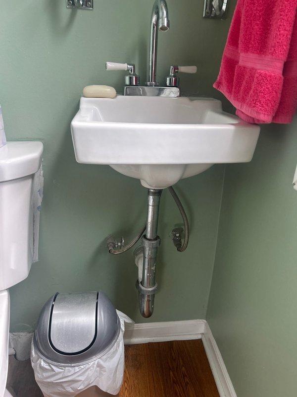 Completed installation of wall-mounted sink with chrome faucet and dual ceramic handle controls in residential bathroom. Installation included proper connection of supply lines through wall-mounted pressure regulator assembly with copper piping, secure mounting of P-trap and drain assembly, and verification of all connections for proper water flow and drainage with no leaks detected.