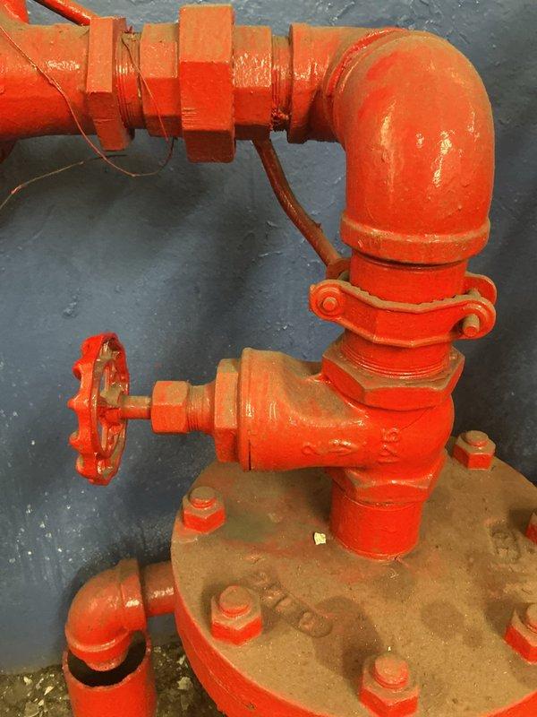 Conducted commercial plumbing inspection of main water valve system following city inspector's request for repair assessment. Inspected underground valve chamber with standing water and submerged valve assembly, documenting deteriorated concrete infrastructure with moisture infiltration and staining. Evaluated fire protection system valve assembly with wheel control handle, flanged connections, and threaded pipe sections, noting corrosion on lower flange and wear on protective coating requiring attention for code compliance.