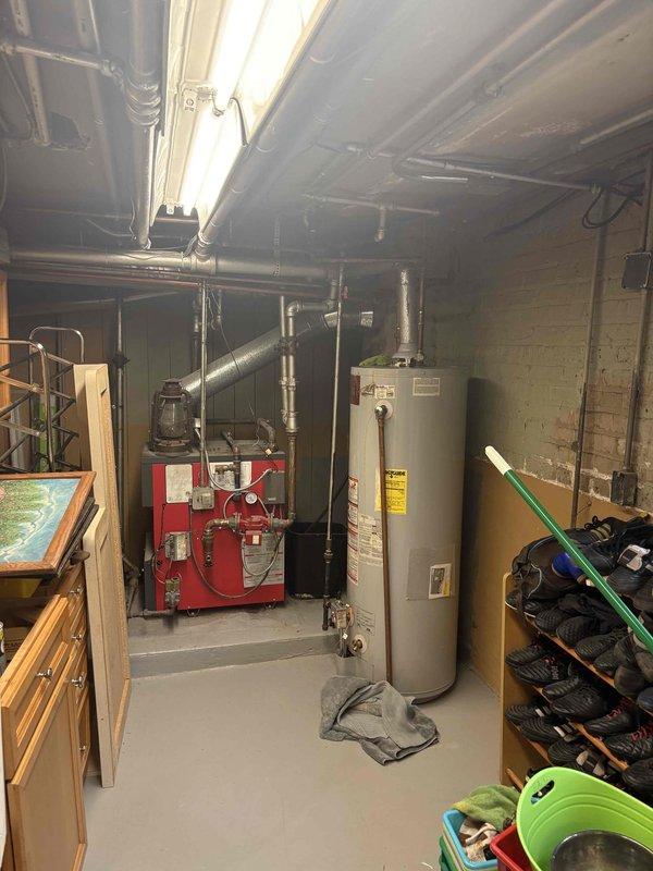 Conducted estimate for water heater replacement in basement of century-old residential property. Assessed existing cylindrical white water heater installation positioned adjacent to red oil-fired boiler system, evaluating current plumbing connections, venting requirements, and accessibility constraints within utility room featuring concrete block walls and exposed ceiling joists. Provided replacement recommendations and pricing options for new water heater installation to meet household hot water demands.
