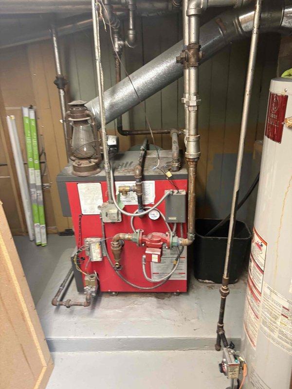Conducted estimate for water heater replacement in basement of century-old residential property. Assessed existing cylindrical white water heater installation positioned adjacent to red oil-fired boiler system, evaluating current plumbing connections, venting requirements, and accessibility constraints within utility room featuring concrete block walls and exposed ceiling joists. Provided replacement recommendations and pricing options for new water heater installation to meet household hot water demands.