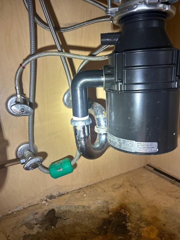 Installed new garbage disposal unit beneath kitchen sink with complete plumbing connections including P-trap configuration and chrome fittings. Documented existing water damage and staining on cabinet floor beneath unit, indicating previous moisture issues that required attention during installation.