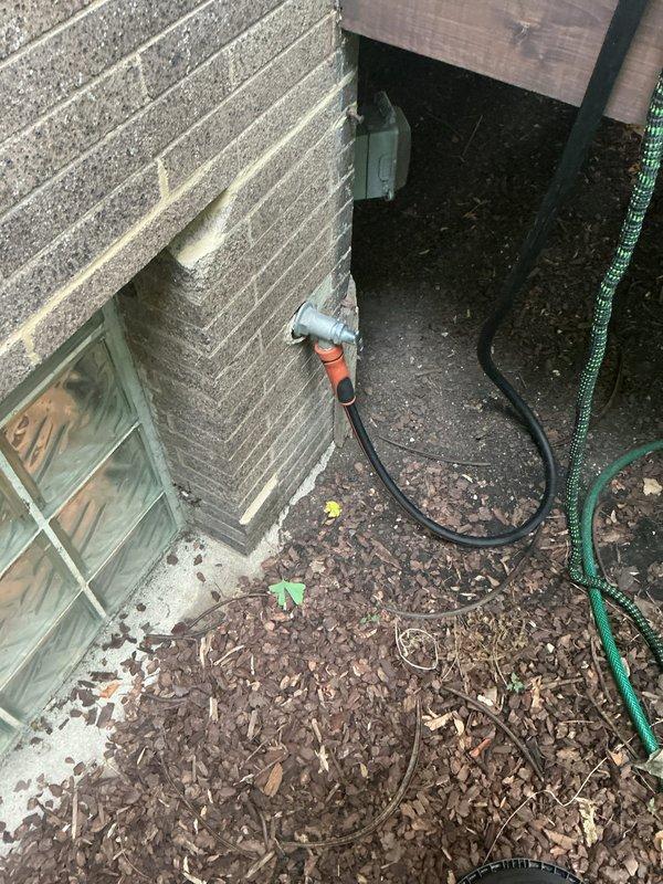 Completed callback service for outdoor hose bib installation. Inspected newly installed galvanized compression-style faucet mounted on exterior wall, verified proper threading and secure connection to orange garden hose, and documented installation with photos showing proper placement and functionality. Confirmed basement window well area utilities and conduit routing were unaffected by the installation work.
