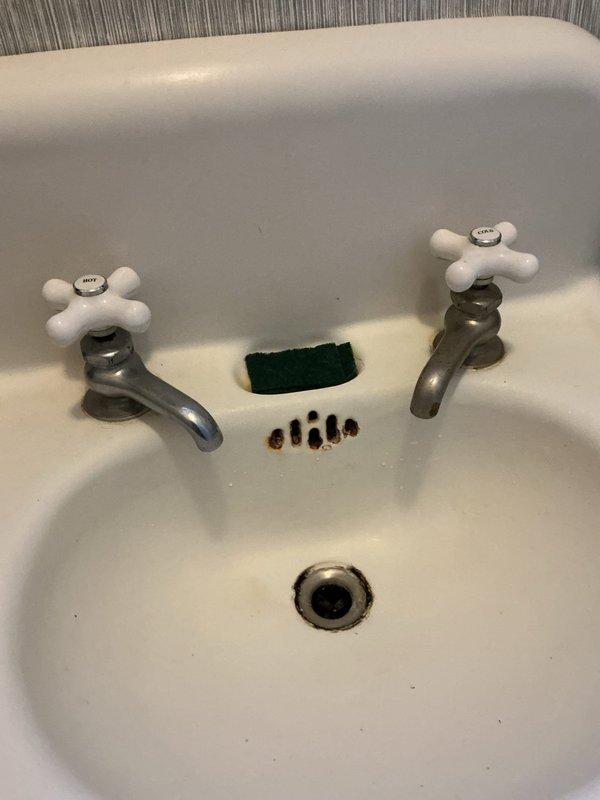 Responded to service request for plumbing inspection beneath bathroom sink. Upon assessment, identified severely corroded metal P-trap with extensive rust deterioration requiring immediate replacement to prevent potential leaks and drainage failures. Documented existing plumbing configuration including shutoff valve and connecting pipes for repair recommendations. Inspected sink basin and drain assembly above, confirming proper drainage function and faucet operation with no visible leaks at fixtures.