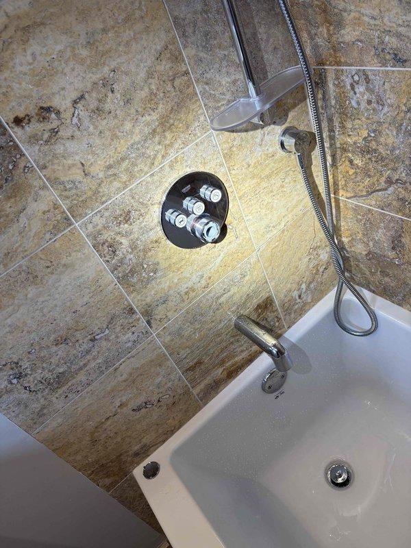 # Shower Faucet Replacement and Fixture Installation

Replaced existing shower faucet assembly with new chrome-plated two-handle fixture on tiled bathroom wall. Removed old mounting hardware and installed new brass mounting assembly with circular escutcheon plate, securing all connections through recessed wall opening. Installed complete shower system including three-valve control configuration with black escutcheon plate, separate volume control knob with decorative flange, and chrome shower arm. Connected handheld shower attachment with braided metal hose and verified proper water flow to both shower head and tub spout. Tested all valve controls for proper hot and cold water operation, checked for leaks at all connection points, and ensured complete functionality of the shower and bathtub system.