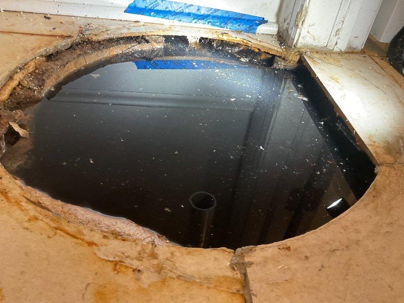 Responded to basement drain clog in 20-year-old residential property. Upon arrival, conducted camera inspection as requested to locate source of blockage. Investigation revealed severe subfloor water damage with significant deterioration around floor drain opening. Found standing water in crawl space beneath compromised plywood subfloor, indicating chronic drainage issue extending beyond initial clog complaint. 

Assessed PVC drainage system configuration and identified failed floor drain assembly as primary concern. Water intrusion had caused extensive structural damage to subfloor materials, requiring removal of deteriorated sections to access affected plumbing components. Documented conditions showing darkly stained and compromised flooring materials, standing water accumulation, and damaged drain infrastructure requiring immediate attention beyond standard drain clearing procedures.

Recommended comprehensive repair plan including subfloor replacement, drain line rehabilitation, an