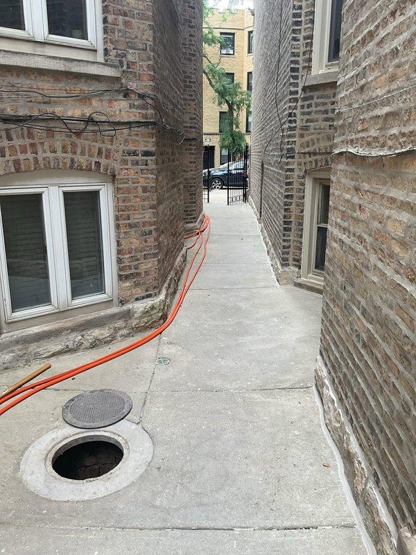 Responded to a drainage backup issue caused by a full catch basin affecting multiple drain points on the property. Upon inspection, located the sewer access point (dated 1995) and adjacent catch basin in the concrete surface area between buildings. The catch basin was found to be completely full with standing water, causing backup conditions through connected drain lines. Deployed equipment through the alleyway access point to address the blockage and restore proper drainage flow. Documented existing conditions showing the flooded catch basin and equipment setup for service records.