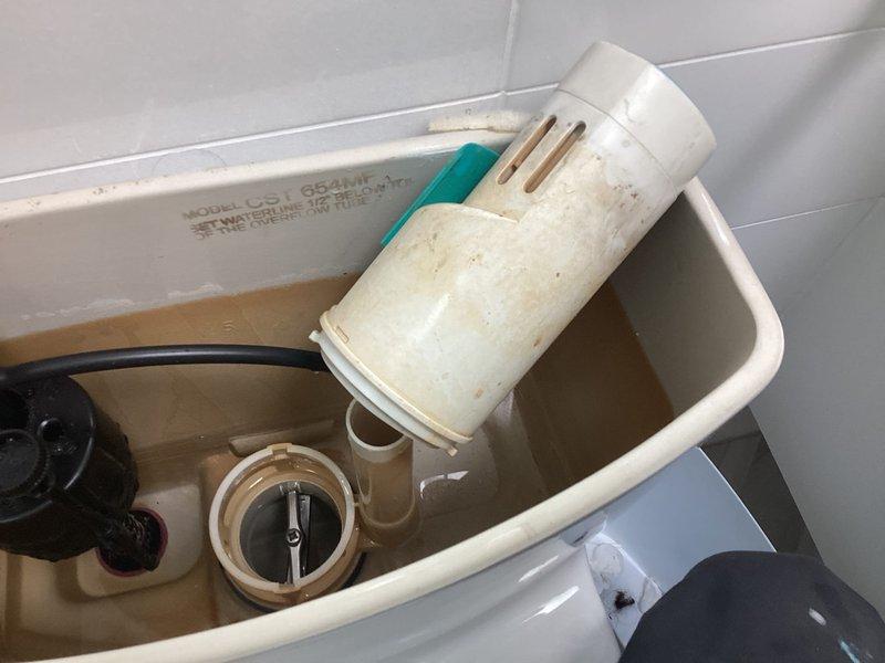 Responded to service call for two toilet issues in a 26-year-old residence with Toto fixtures. Successfully cleared clog on first-floor toilet that had been non-functional for three days. Inspected second-floor toilet with continuous running issue ongoing for several weeks; removed tank lid and identified worn flapper valve assembly showing discoloration and mineral buildup, along with aged fill valve components displaying brown staining and sediment accumulation. Photographed internal tank mechanisms documenting condition of flush valve, flapper, fill valve, and overflow tube. Water in tank exhibited brownish discoloration indicating mineral content and system age, consistent with original plumbing components in service for over two decades.
