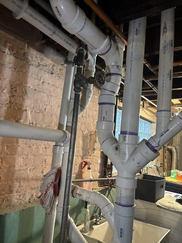 Completed financing arrangement for comprehensive plumbing system installation in basement mechanical room. New system includes boiler unit, sump pump with containment basin, water heater, and extensive PVC piping network with multiple branch connections throughout the space, requiring scheduling for final installation phase.