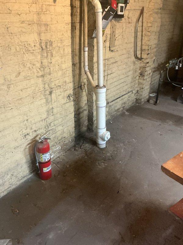Responded to basement flooding issue caused by rainwater intrusion with standing water present. Assessed existing drainage system including vertical PVC piping configuration along foundation walls. Evaluated structural conditions in basement area, noting water damage patterns and moisture infiltration points at floor-wall junctions. Documented plumbing infrastructure and recommended overflow protection system installation to prevent future flooding events during heavy precipitation.