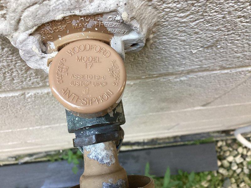 Responded to a heavy water leak at an exterior hose spigot equipped with a Woodford Model 17 anti-siphon valve. Upon inspection, found significant mineral deposits and weathering around the backflow prevention device, indicating prolonged exposure to leaking water. Replaced the faulty valve assembly with new brass fittings and installed proper flow control components to restore functionality and prevent future water waste.