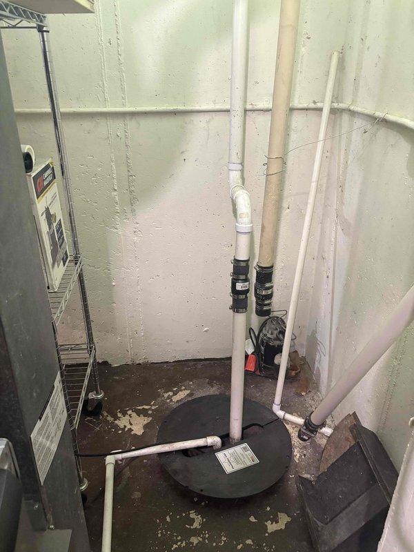 Responded to service call for leaking cast iron sewer pipe in basement of 50-year-old residential property. Upon arrival, conducted thorough inspection of existing plumbing system and identified minor leak in aging cast iron waste line. Assessed overall condition of basement plumbing infrastructure, including vertical PVC drain lines and waste pipe connections visible along foundation walls. Documented existing pipe configuration with multiple vertical runs, rubber coupling connections, and various junction points. Evaluated floor conditions around plumbing area, noting deteriorated surface coating and potential moisture concerns related to leak. Inspected sump pump system as requested, including examination of pump basin cover and surrounding drainage components. Provided consultation regarding sump pump operation, maintenance requirements, and recommendations for basement moisture management. Photographed existing plumbing conditions for reference, showing current PVC installation, p